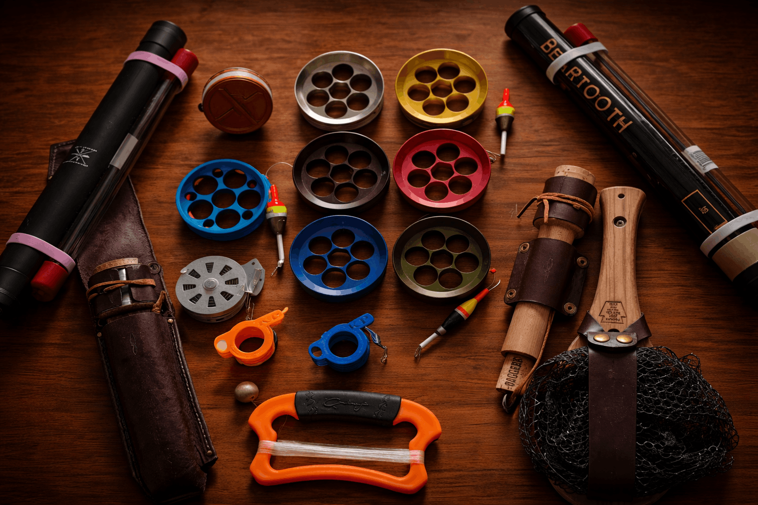 Flat-lay of handline fishing reels and accessories — colorful discs, cases, floats, and nets on a dark wood surface